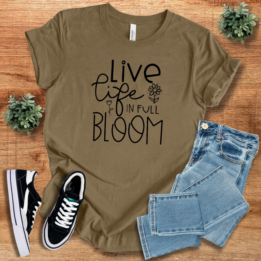 Olive brown 'Live Life in Full Bloom' t-shirt with black floral typography, styled with denim jeans and sneakers. A sustainable, regular-fit cotton tee for everyday fashion.
