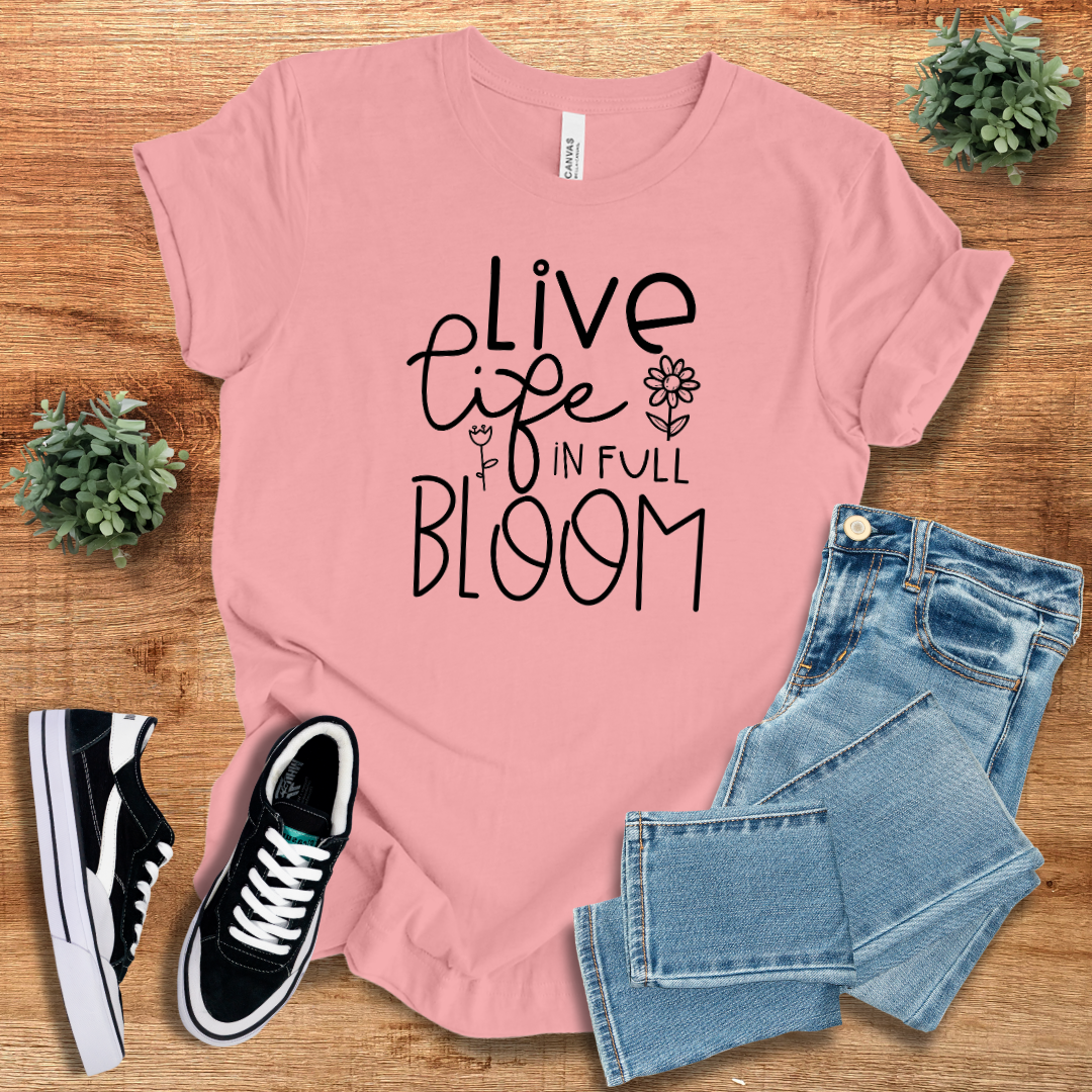 Pink 'Live Life in Full Bloom' t-shirt featuring black floral typography, paired with denim jeans and sneakers. A stylish, eco-friendly cotton tee for everyday comfort.