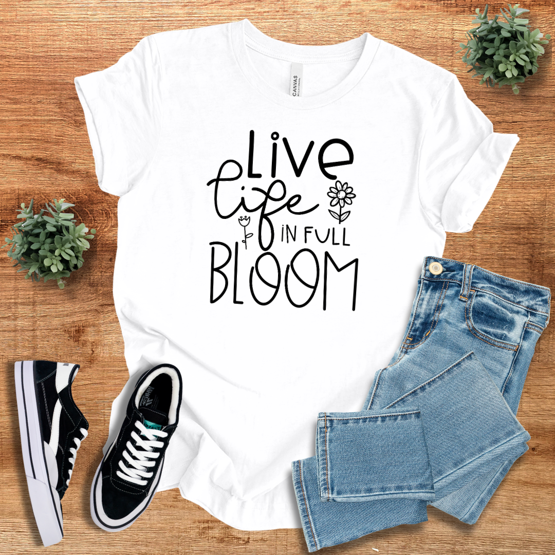 White 'Live Life in Full Bloom' t-shirt with black floral typography, styled with denim jeans and sneakers. A lightweight, unisex cotton tee for versatile fashion.
