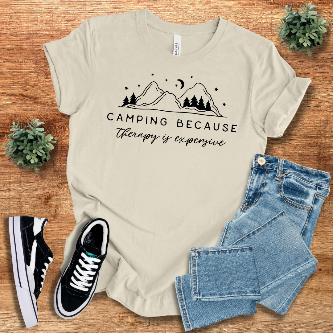 Beige 'Camping Because Therapy is Expensive' T-shirt with a minimalist mountain and tree print. Breathable cotton tee for outdoor enthusiasts.