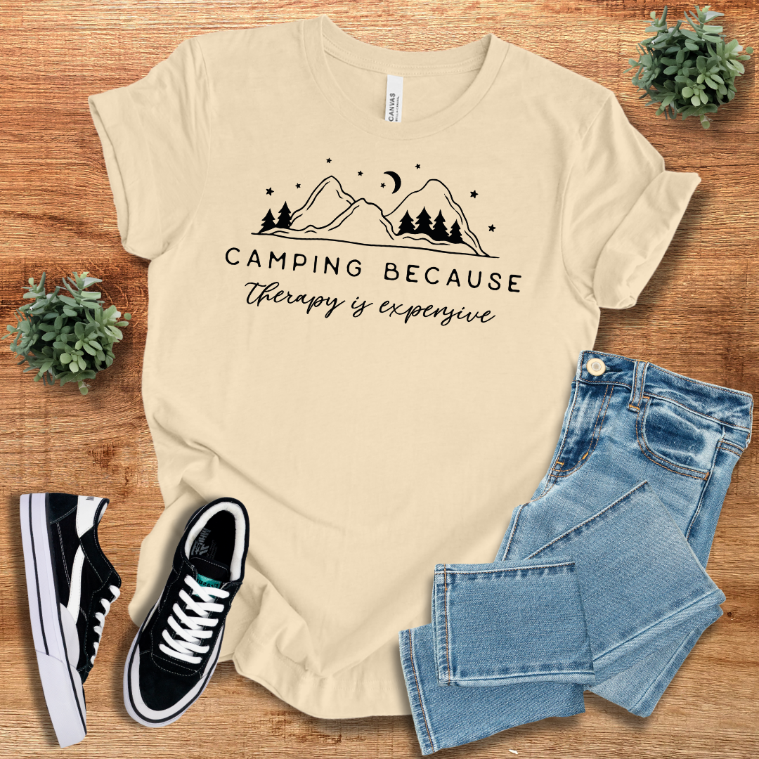 Cream 'Camping Because Therapy is Expensive' T-shirt featuring a mountain and tree print. Comfortable and stylish unisex tee for outdoor lovers.