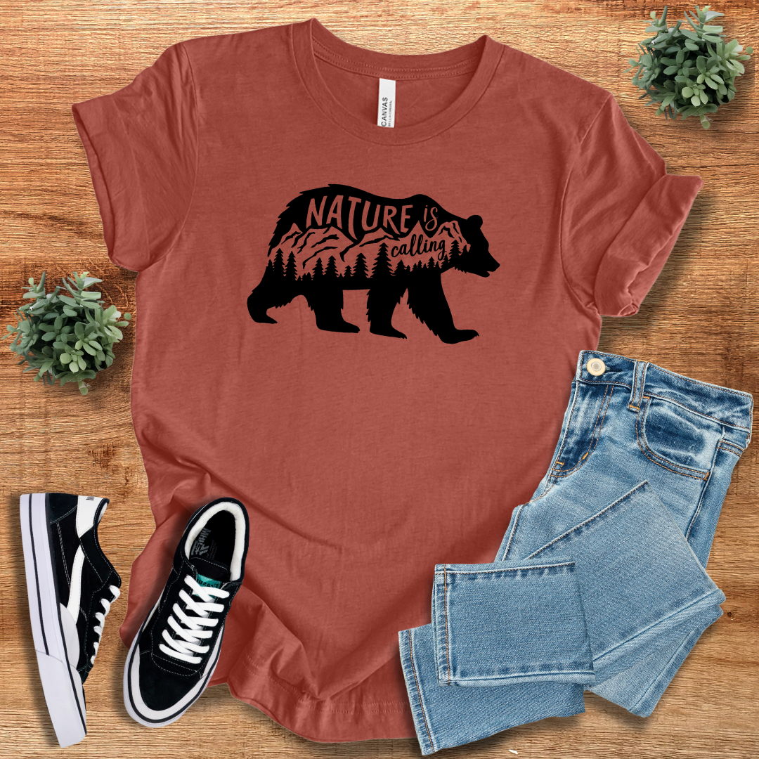Brick red 'Nature Is Calling' t-shirt with a black bear silhouette and scenic mountain design. A comfortable and stylish outdoor wear option.