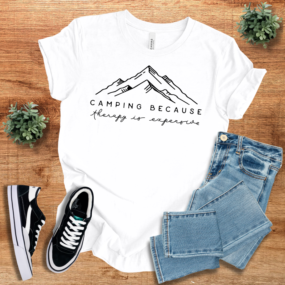 White 'Camping Because Therapy is so Expensive' t-shirt featuring a minimalist mountain print. Soft cotton crew neck tee for hiking and everyday wear.