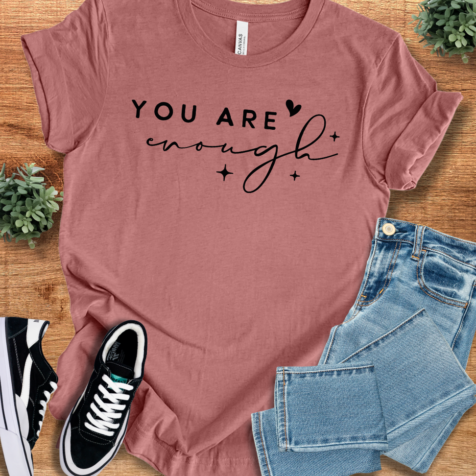 Mauve 'You Are Enough' unisex cotton t-shirt with black script text, laid flat with jeans and sneakers. Soft, ethical fashion statement tee.