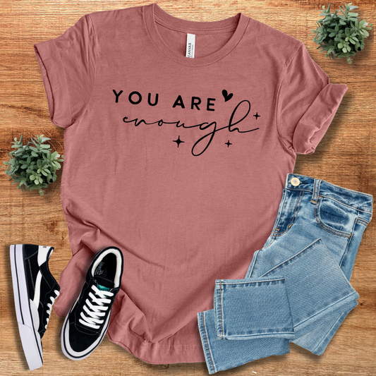 Mauve 'You Are Enough' unisex cotton t-shirt with black script text, laid flat with jeans and sneakers. Soft, ethical fashion statement tee.