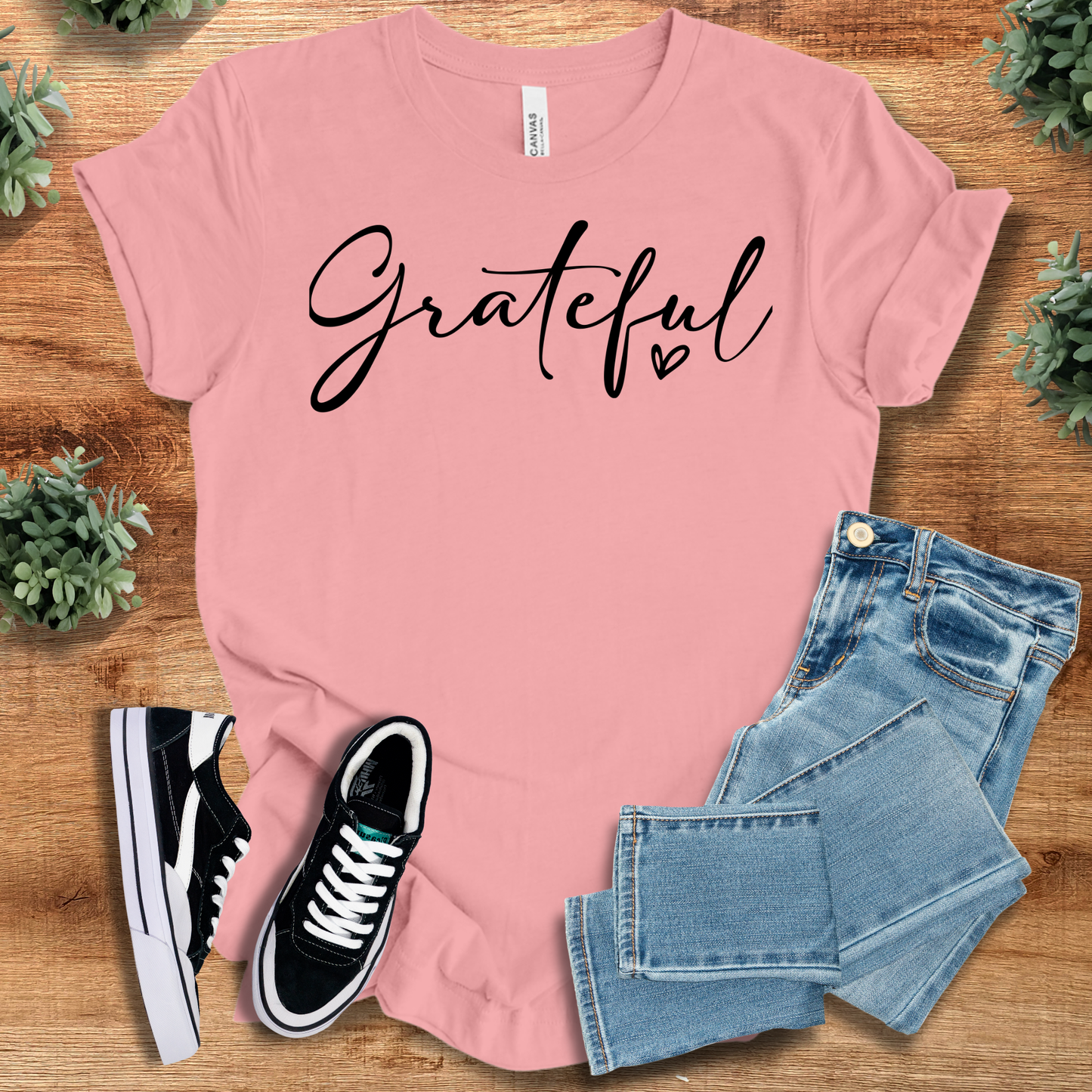 White t-shirt with '' text, flat lay styled on a wooden surface.
