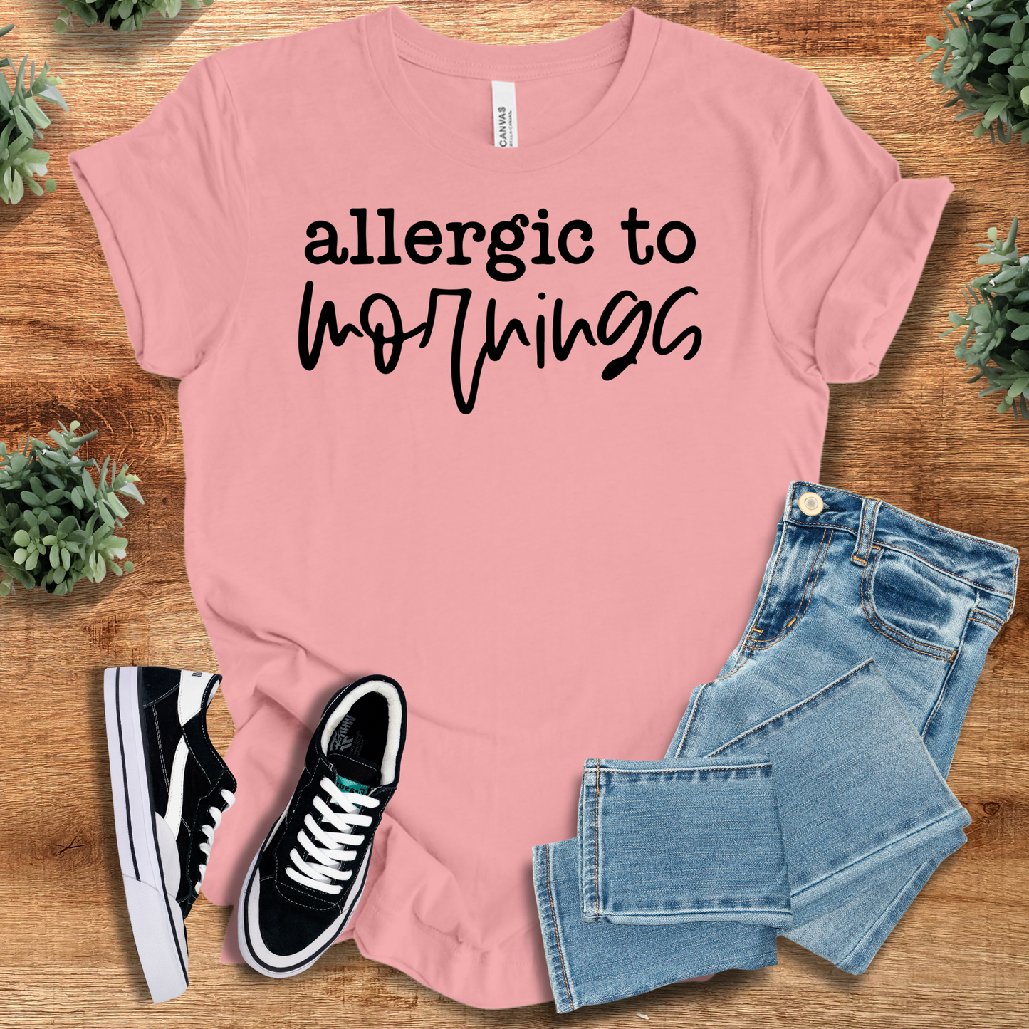 Pink t-shirt with '' text, flat lay styled on a wooden surface.
