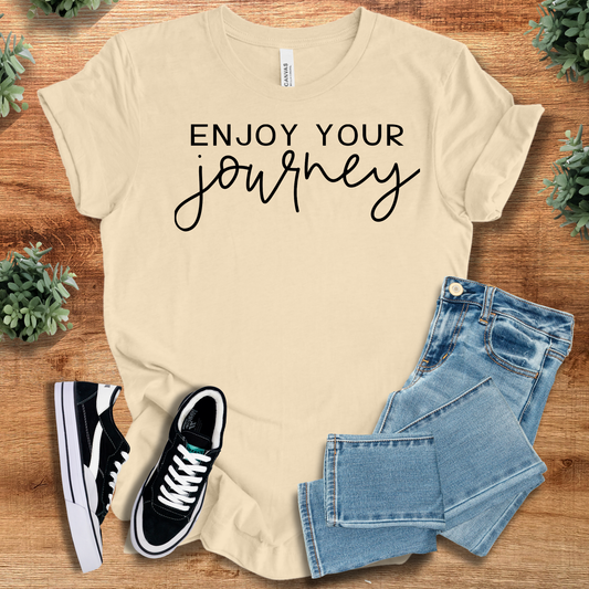Enjoy Your Journey - Positive Journey T-Shirt in beige with black script, styled with jeans and sneakers. 100% cotton travel-themed tee.