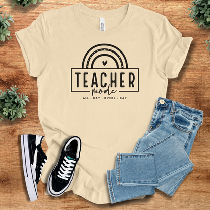 Soft-cream t-shirt with 'Teacher Mode T‑Shirt' text, flat lay styled on a wooden surface.