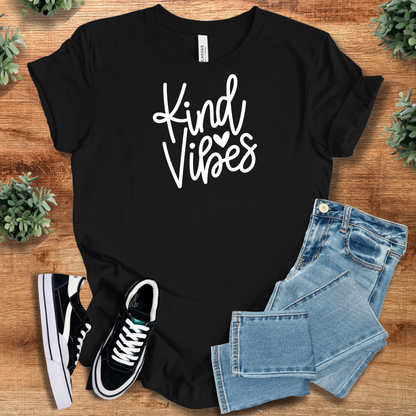 Black t-shirt with 'Kind Vibes Tee T‑Shirt' text, flat lay styled on a wooden surface.