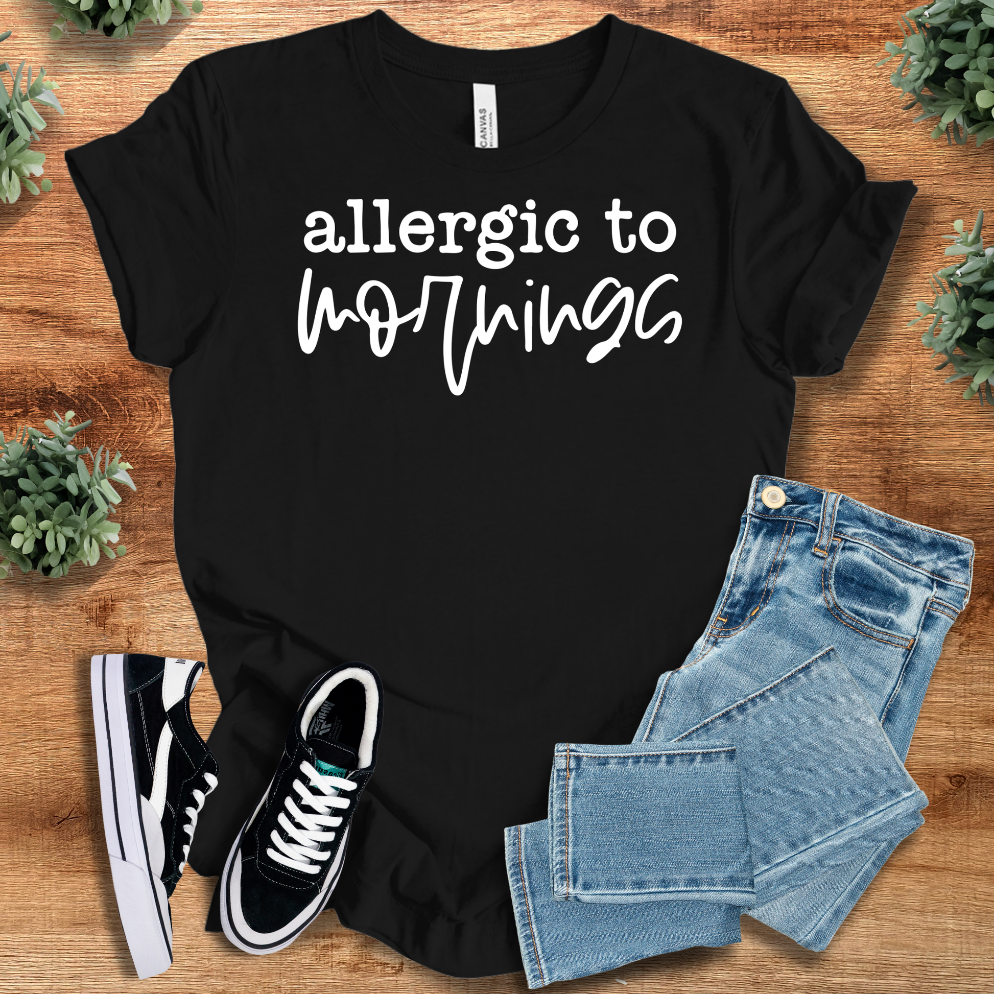 Black t-shirt with 'Allergic to Mornings Tee' text, flat lay styled on a wooden surface.