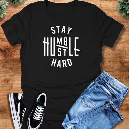 Black t-shirt with 'Stay Humble Hustle Hard T‑Shirt' text, flat lay styled on a wooden surface.