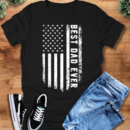 Black t-shirt with 'Best Dad Ever Flag T‑Shirt' text, flat lay styled on a wooden surface.