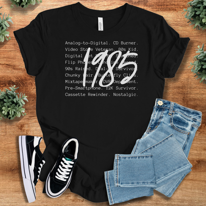 Black t-shirt with '1985 Tee - Vintage Retro Style' text, flat lay styled on a wooden surface.