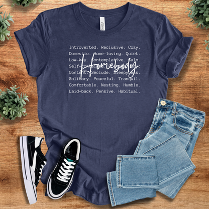 Heather-navy t-shirt with 'Homebody Definition T‑Shirt' text, flat lay styled on a wooden surface.