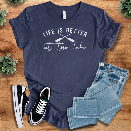 Heather-navy t-shirt with 'Life Is Better At The Lake T‑Shirt' text, flat lay styled on a wooden surface.