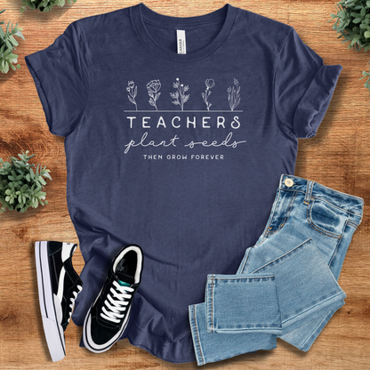 Heather-navy t-shirt with 'Teachers Plant Seeds T‑Shirt' text, flat lay styled on a wooden surface.