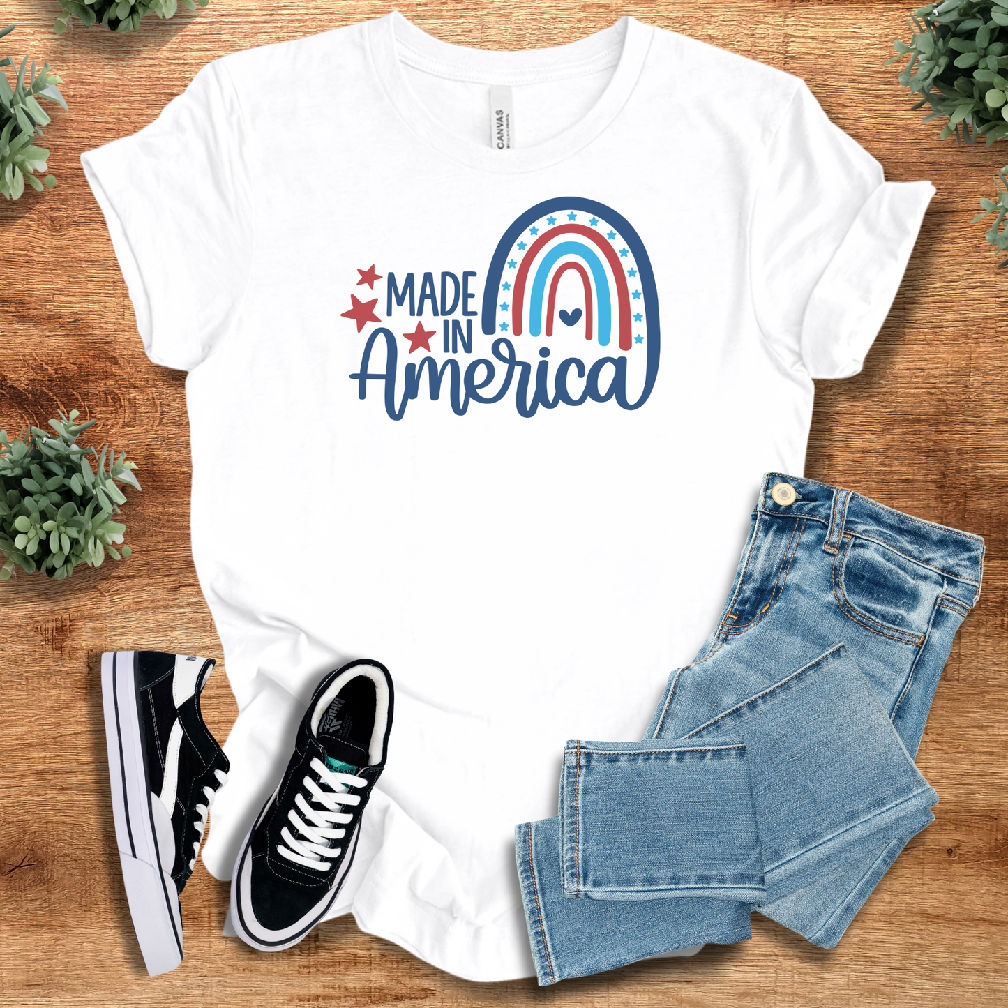 White t-shirt with 'Patriotic Made In America T‑Shirt' text, flat lay styled on a wooden surface.