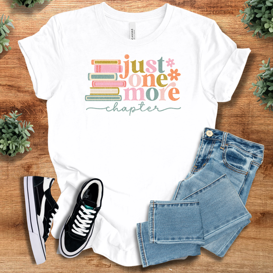 Just One More Chapter unisex book lover t-shirt in white with colorful stacked books design. Ideal for bibliophiles and casual reading wear.
