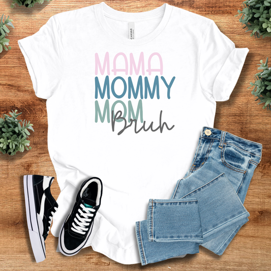 White t-shirt with 'Mama, Mommy, Mom, Bruh Tee' text, flat lay styled on a wooden surface.