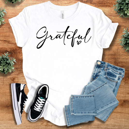 White t-shirt with 'Grateful Tee' text, flat lay styled on a wooden surface.